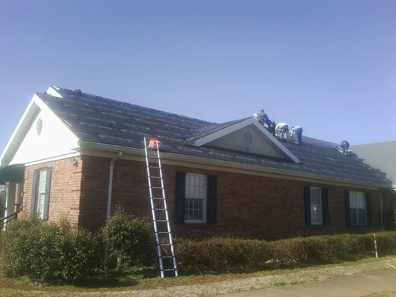 Crew tearing shingles off a brick ranch roof with a ladder set — Metal Roof Repair work by our crew in Granville