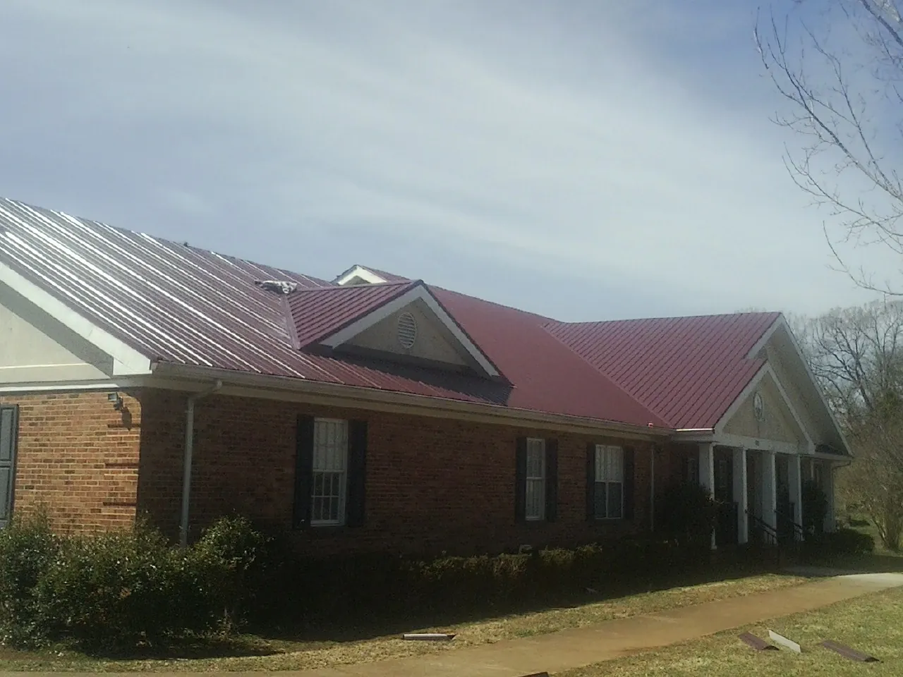 Red metal roof with gabled entries on a long brick building, from a Hail Damage Roof Repair job in Granville